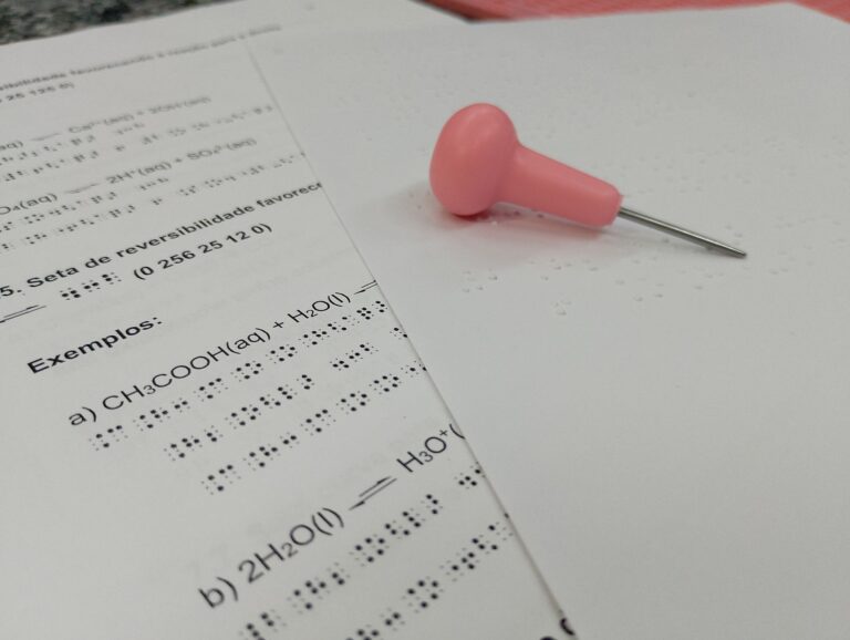 Braille chemistry sheet with pink pin for tactile learning.