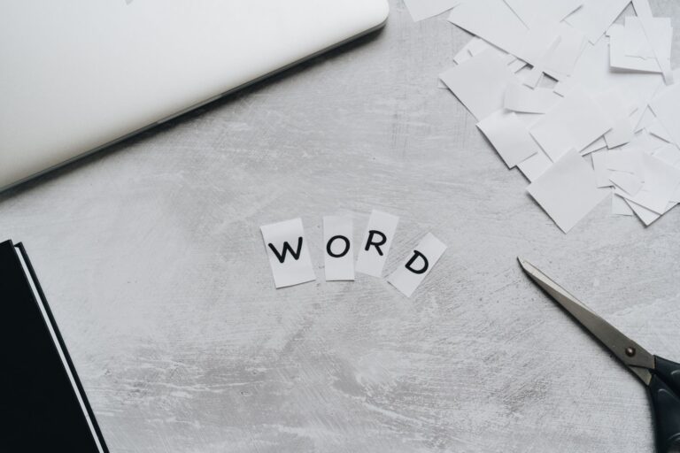 Top view of a workspace with scattered paper letters spelling 'WORD', next to a laptop and scissors.