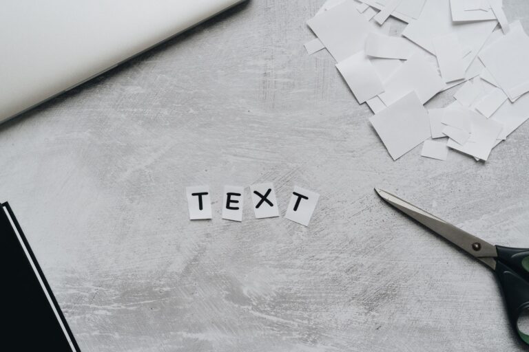 A flat lay of a creative workspace featuring cutout text, scissors, and paper pieces on a textured surface.